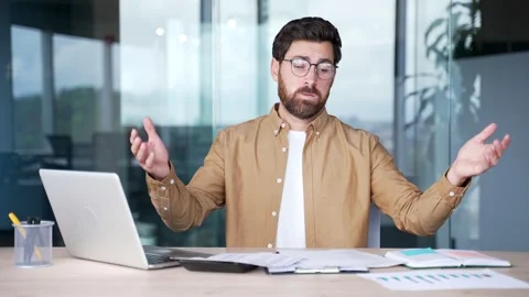 Confused businessman having difficulty with paperwork sitting at desk Stock Footage 325513096