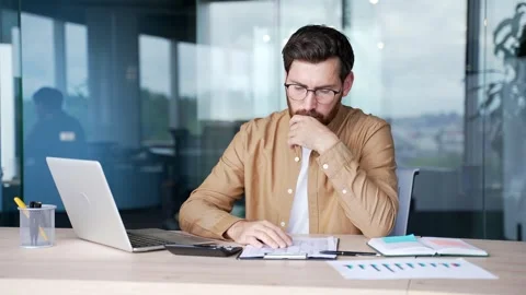 Confused businessman having difficulty with paperwork sitting at desk  Stock Footage 325513124