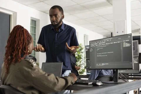Confused developer discussing coding scripts with female coworker Foto stock