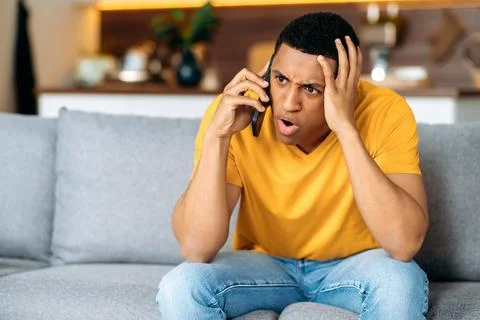 Confused hispanic guy sitting on the couch in the living room, dressed in casual Fotos Stock