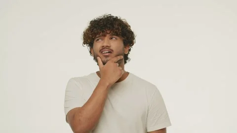 Confused Indian guy touching his beard. Studio footage of bewildered young man Stock Footage 231674072