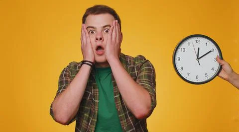 Confused man with anxiety checking time on clock, running late to work, being in Stock Photos