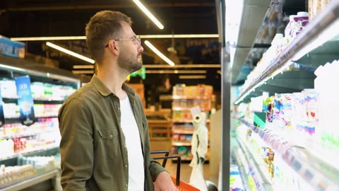 A confused man cannot choose dairy products in the supermarket Stock Footage 244576875