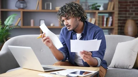 Confused man having difficulty with paper work using laptop computer sitting  Stock Footage 297873367