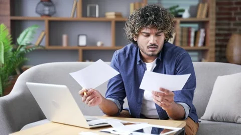 Confused man having difficulty with paper work while sitting at home office.  Видео 334228189