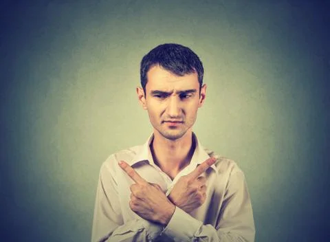 Confused man pointing in two different directions, hesitant to make decision Stock Photos