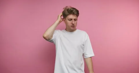 Confused man trying to solve a puzzle in front of a pink wall at home Stock Footage 317327951