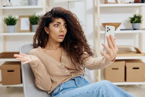 Confused unhappy irritated shocked tanned curly Latin lady have video call hold Stock Photos