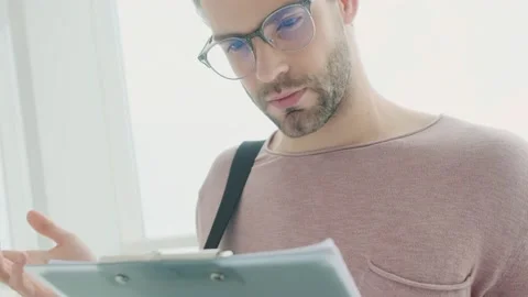 Confused young bearded man is reading the documents standing near the window Stock Footage 133343759