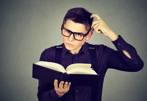 Confused young man in glasses perplexed after reading a book Stock Photos