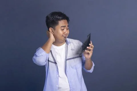A confused young man scratching the back of his neck while looking at his e.. Stock Photos