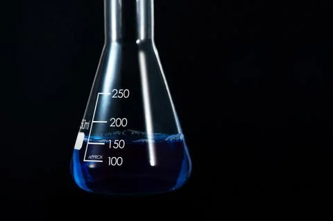 A conical flask filled with a blue solution on a black background Stock Photos