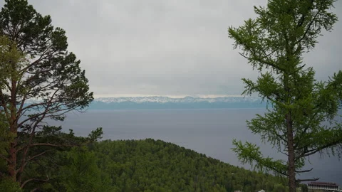 Coniferous trees frame scenic view of lake Baikal with snow-capped Sayan Stock Footage 315002868