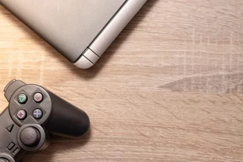 Console gaming controller and a silver laptop on a brown grey wooden surface. Stock Photos