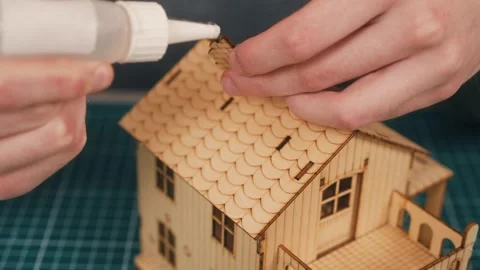 Constructing wooden house model with hands attaching chimney piece using glue Stock Footage 336309819