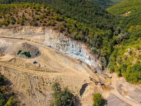 Construction and mining activity at a hillside site near a forest in daylight Stock Photos