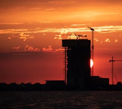 Construction and sky-scraper building and crane against colorful sky with sun Stock Photos