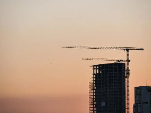 Construction and sky-scraper building and crane against colorful sky with sun. Stock Photos