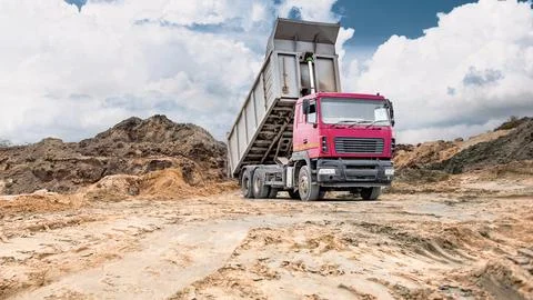 Construction area features dry cracked earth and dirt mounds while a truck un 스톡 사진