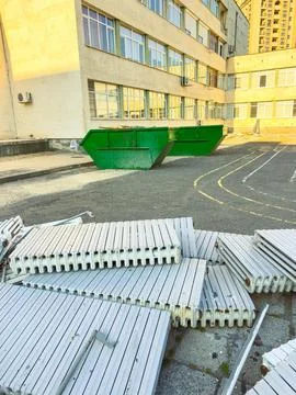 Construction area shows a green dumpster and stacked materials near a large.. Stock Photos
