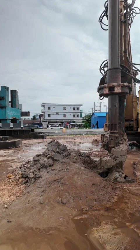 Construction auger drills into muddy ground at a work site, pulling up wet soil. Stock Footage 336763560