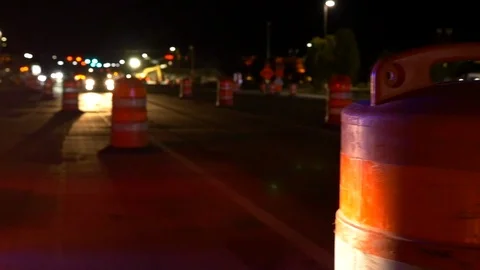 Construction barrel in foreground with traffic speeding by at night. Video stock 99517999