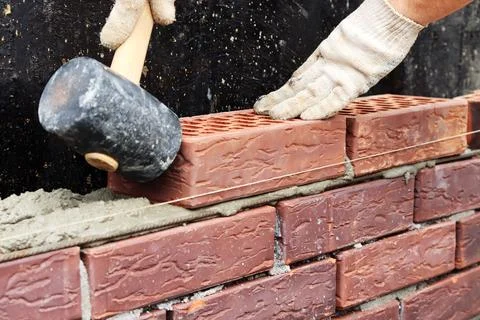 Construction of a brick wall. Brick laying. Hand in a glove and a hammer Stock Photos