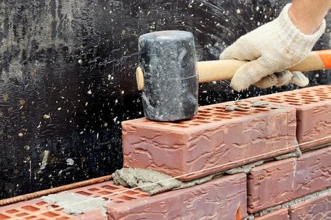 Construction of a brick wall. Brick laying. Hand in a glove and a hammer Stock Photos