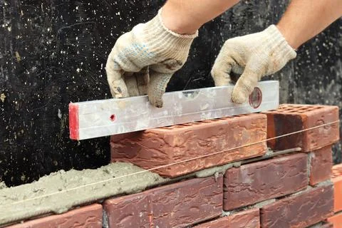 Construction of a brick wall. Checking the evenness of the wall. Gloved hands Stock Photos