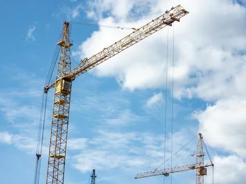 Construction concept. Tower cranes against a bright blue sky with clouds Stock Photos