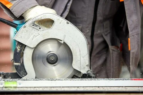 A construction contractor worker using a worm-driven hand-held circular saw to Stock Photos