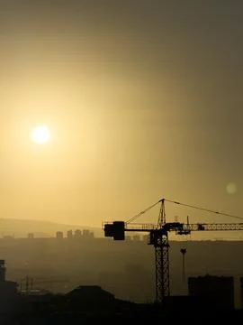 Construction crane against the backdrop of a city with a bright sun . A crane is Stock Photos