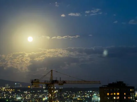 Construction crane against the backdrop of a night city with a bright moon. A Stock Photos