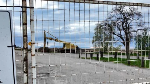 Construction crane and bare tree behind wire fence on a cloudy day outdoors Stock Footage 315622942