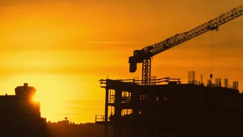 Construction crane and building framework silhouetted against the sunset over a Stock Footage 348295003