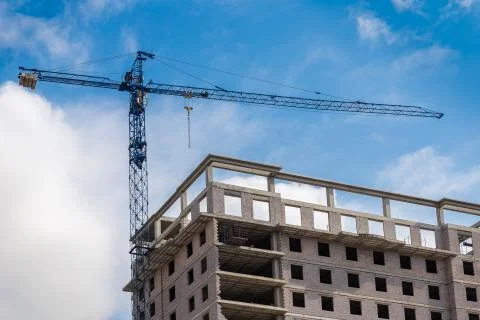 Construction crane and skyscraper building on background of blue sky with clouds Stock Photos