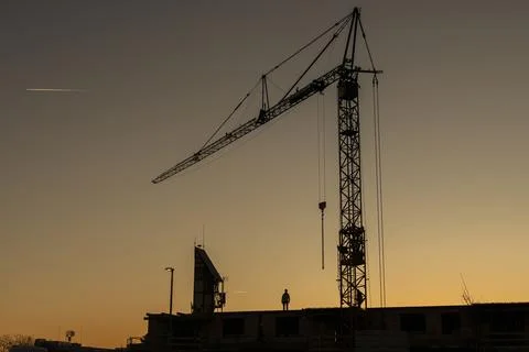 Construction Crane and Worker Silhouette Against Sunset Sky Foto stock
