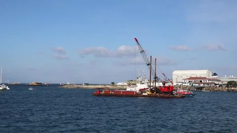 Construction Crane Barge Operating in a Coastal Harbor with Buildings Stock Footage 344977247