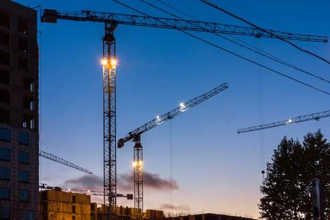 Construction crane in the city while working in new buildings. Evening city l Stock Photos