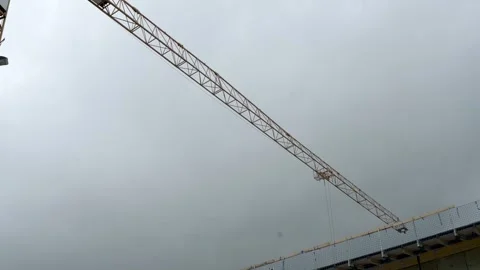 A construction crane extending over a building site with a cloudy sky background Vidéo 281536129