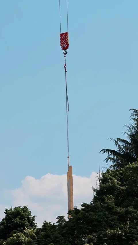 Construction crane lifting heavy load against blue sky and trees Stock Footage 334632619