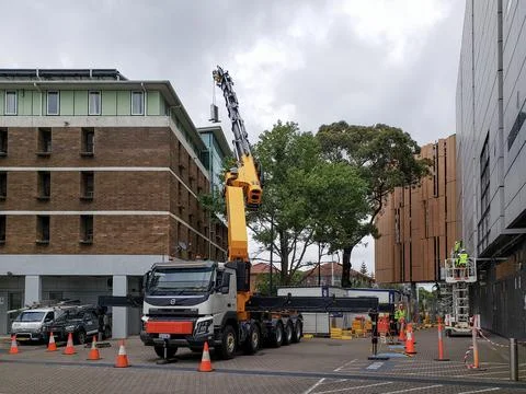 Construction crane lifting a heavy payload over a building block Stock Photos