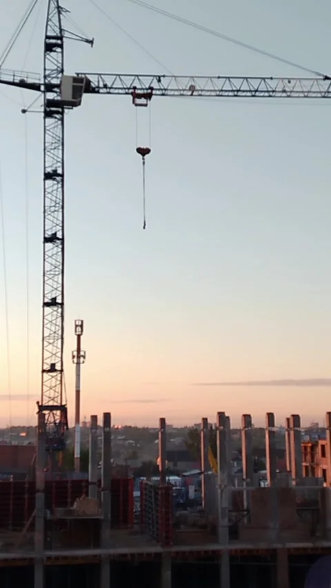Construction crane lifting materials at building site during sunset with city Stock Footage 340606536