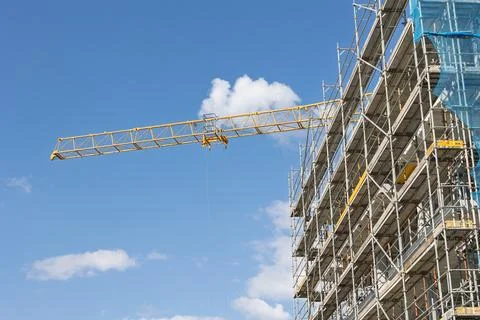 Construction crane lifting materials at building site with scaffolding Stock Photos