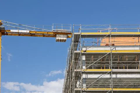 Construction crane lifting materials at building site with scaffolding Stock Photos