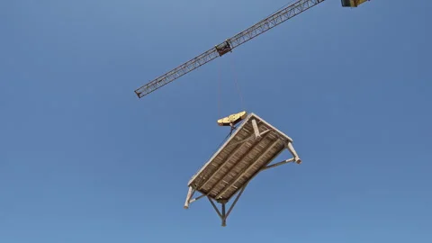 Construction Crane Lifting Wooden Platform Against Clear Blue Sky, Elevated Vidéo 312443561