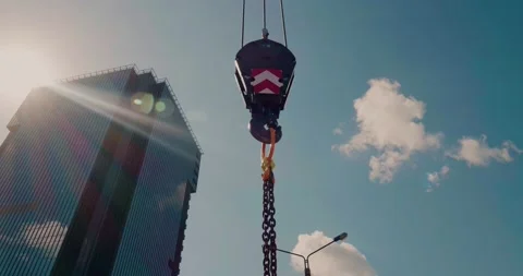 A construction crane lifts a load with a hook and chains against the skyscraper Stock Footage 136842659