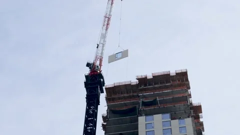 Construction crane moving a window frame towards construction workers. Stock-Footage 151488656