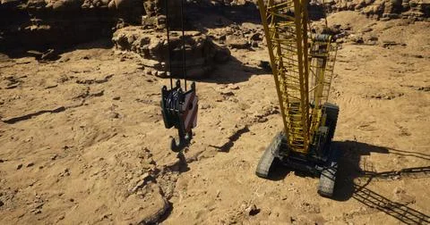 Construction crane operates in rugged terrain during daylight hours Illustrazione stock