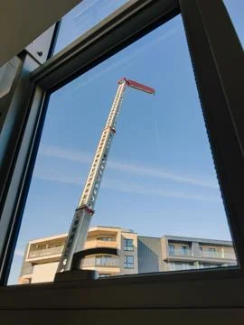 Construction crane operating on building site, framed by window of modern Foto stock
